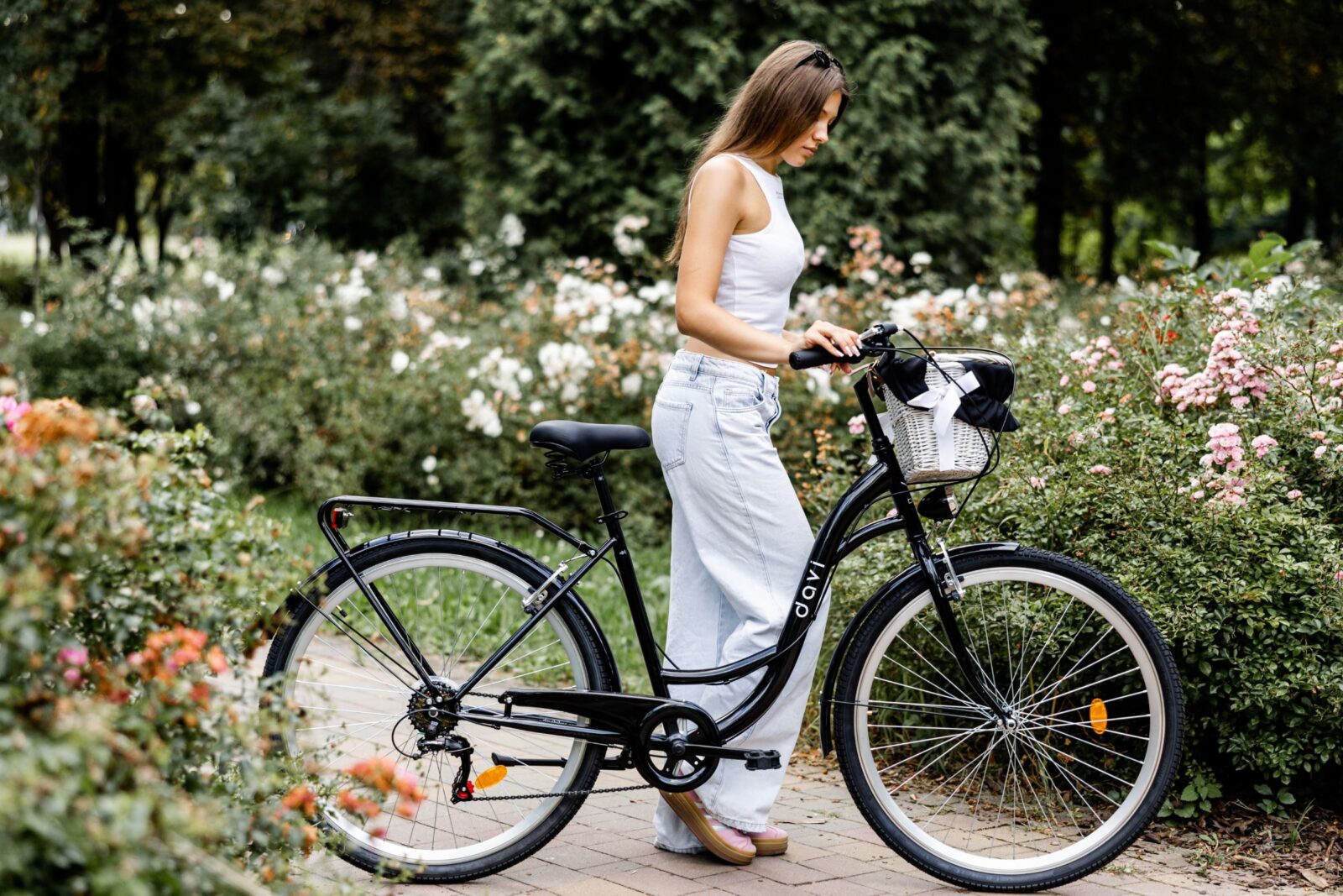 Kvinna med cykel bland blommor i parken