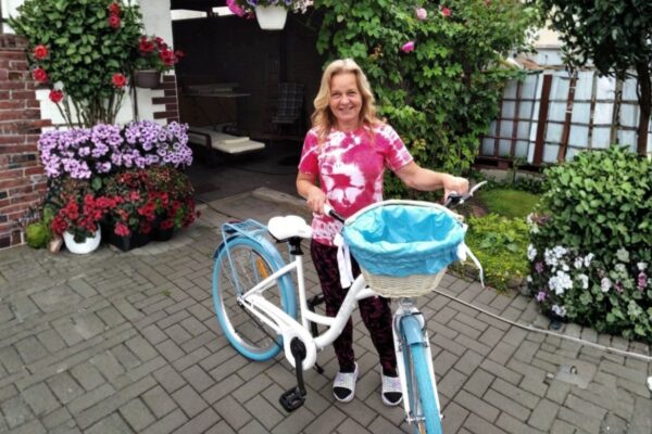 Kvinna med cykel framför blommor vid hus